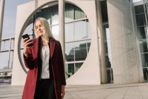 Blond businesswoman using smartphone in the background modern building — Stock Photo