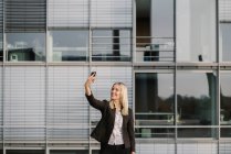 Blond businesswoman using smartphone and taking a selfie — Stock Photo