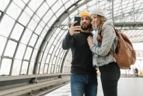 Feliz pareja joven usando smartphone en la plataforma de la estación, Berlín, Alemania - foto de stock