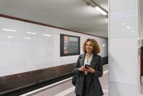 Smiling woman with cell phone waiting in subway station — Stock Photo