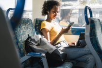 Young woman with earphones using smartphone and tablet on a train — Stock Photo