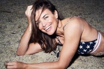 Ritratto di donna attraente ridente che indossa bikini sdraiato nella sabbia — Foto stock