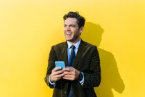 Felice uomo d'affari con smartphone davanti alla parete gialla — Foto stock