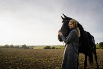 Zärtliche junge Frau mit Pferd auf einem Feld auf dem Land — Stockfoto