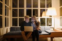 Coppia anziana che utilizza il computer portatile sul divano a casa di notte — Foto stock