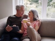 Felice coppia anziana relax sul divano a casa utilizzando tablet per lo shopping online — Foto stock