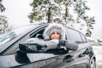 Portrait de jeune femme souriante penchée par la fenêtre de la voiture dans la forêt d'hiver — Photo de stock