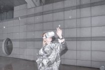 Menina em terno de prata olhando através de óculos VR, observando sua mão — Fotografia de Stock