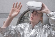 Menina em terno de prata olhando através de óculos VR, observando sua mão — Fotografia de Stock