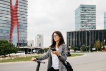 Young businesswoman using smartphone standing on e-scooter in the city — Stock Photo