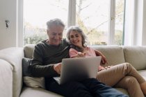 Felice coppia anziana con computer portatile rilassante sul divano a casa — Foto stock