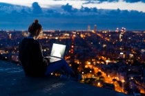 Young woman using laptop at dawn above the city, Barcelona, Spain — Stock Photo