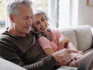 Felice coppia anziana con computer portatile rilassante sul divano a casa — Foto stock