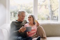 Felice coppia anziana relax sul divano a casa utilizzando tablet per lo shopping online — Foto stock