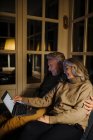 Couple aîné utilisant un ordinateur portable sur le canapé à la maison la nuit — Photo de stock