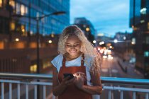 Young woman in the city at dusk looking at her smartphone — Stock Photo