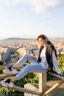 Jeune femme assise sur une rampe au-dessus de la ville en utilisant un téléphone portable, Barcelone, Espagne — Photo de stock