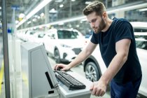 Hombre trabajando en la computadora en la fábrica de automóviles modernos - foto de stock
