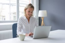 Lächelnde junge Geschäftsfrau benutzt Laptop am Schreibtisch im Büro — Stockfoto