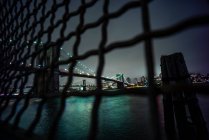 Estados Unidos, Nueva York, Ciudad de Nueva York, cerca de alambre contra el iluminado puente de Brooklyn por la noche - foto de stock
