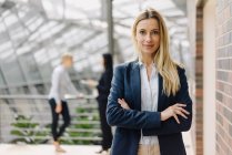 Portrait of a confident young businesswoman in a modern office building with colleagues in background — Stock Photo