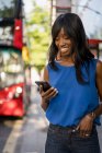 Femme afro-américaine utilisant un smartphone à l'arrêt de bus à Londres, Royaume-Uni — Photo de stock