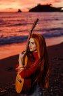Porträt einer rothaarigen jungen Frau mit Gitarre am Strand bei Sonnenuntergang mit Fernblick, Almunecar, Spanien — Stockfoto