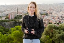 Portrait of smiling young woman with camera at sunrise above the city, Barcelona, Spain — Stock Photo