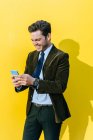 Felice uomo d'affari utilizzando smartphone di fronte alla parete gialla — Foto stock