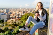 Giovane donna seduta sulla ringhiera sopra la città con il cellulare in mano, Barcellona, Spagna — Foto stock