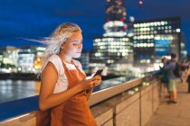 Young woman in the city at dusk looking at her smartphone — Stock Photo