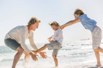 Отец веселится со своими сыновьями на пляже, бегает и прыгает в песок — стоковое фото