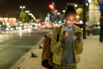Portrait de contenu jeune femme utilisant des écouteurs et smartphone dans la ville la nuit, Lisbonne, Portugal — Photo de stock
