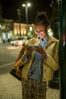 Portrait of smiling young woman using earphones and smartphone in the city by night, Lisbon, Portugal — Stock Photo