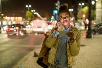 Portrait de jeune femme utilisant écouteurs et smartphone dans la ville la nuit, Lisbonne, Portugal — Photo de stock