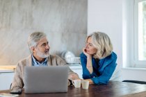 Mature man with wife using laptop on kitchen table at home — Stock Photo