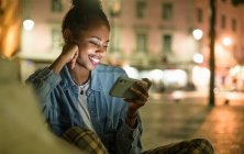 Portrait of happy young woman using smartphone in the city by night, Lisbon, Portugal — Stock Photo