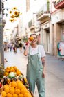 Retrato de la joven riendo en la calle comercial cubriendo el ojo con una naranja - foto de stock