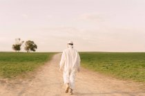 Rear view of man wearing protective suit walking on dirt track in the countryside — Stock Photo