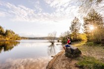 Sportive man sitting on a rock at the lakeside at sunset, Forstsee, Carinthia, Austria — Stock Photo