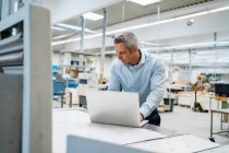 Uomo d'affari che utilizza il computer portatile in fabbrica — Foto stock