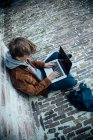 Adolescente che utilizza il computer portatile e seduto su un pavimento di pietra in città — Foto stock