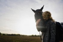 Привітна молода жінка з конем на полі в сільській місцевості при заході сонця. — стокове фото