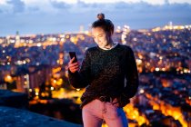 Jeune femme assise sur une rampe au-dessus de la ville en utilisant un téléphone portable, Barcelone, Espagne — Photo de stock