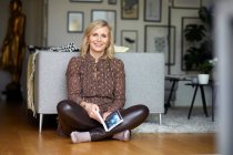 Портрет усміхненої блондинки відпочиває вдома, сидячи на підлозі. — стокове фото