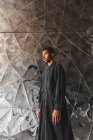 Молодий чоловік у чорному кафті стоїть на структурованій стіні — стокове фото