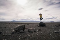 Зрелый человек балансирует на одной ноге на скале в вулканическом высокогорье Исландии — стоковое фото