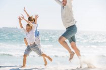 Отец веселится со своими сыновьями на пляже, бегает и прыгает в песок — стоковое фото