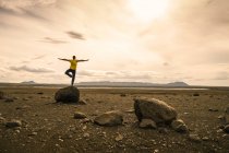 Зрелый человек балансирует на одной ноге на скале в вулканическом высокогорье Исландии — стоковое фото