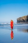 Mujer rubia vestida de rojo y sombrero y caminando por la playa, Playa de Las Catedrales, España - foto de stock